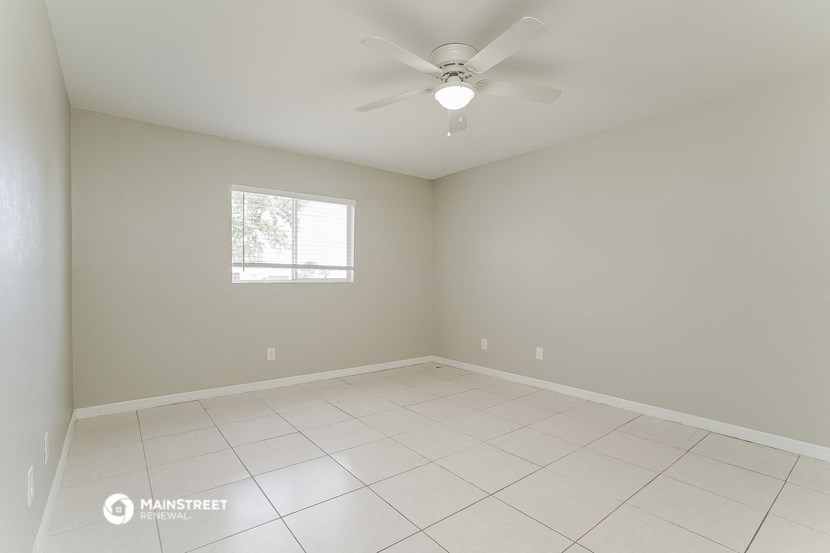 the spacious living room has a ceiling fan and tiled floors