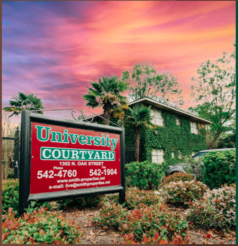 a sign in front of a house with palm trees