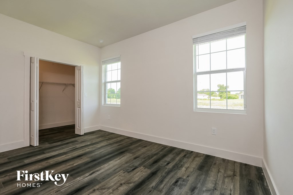 a bedroom with white walls and wood flooring and a closet