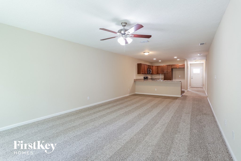 an empty living room with a ceiling fan and a kitchen