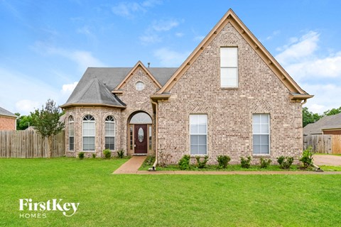 a brick house with a green lawn and a wooden fence