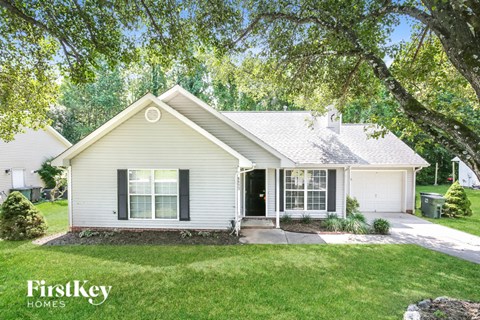 A house with a white siding and a black door is surrounded by greenery.