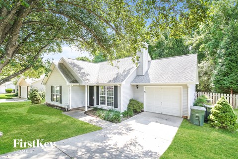 A white house with a garage is surrounded by greenery.