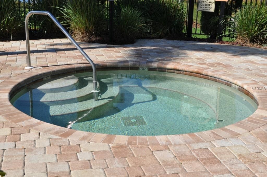 A hot tub with a metal staircase is surrounded by brick pavers.