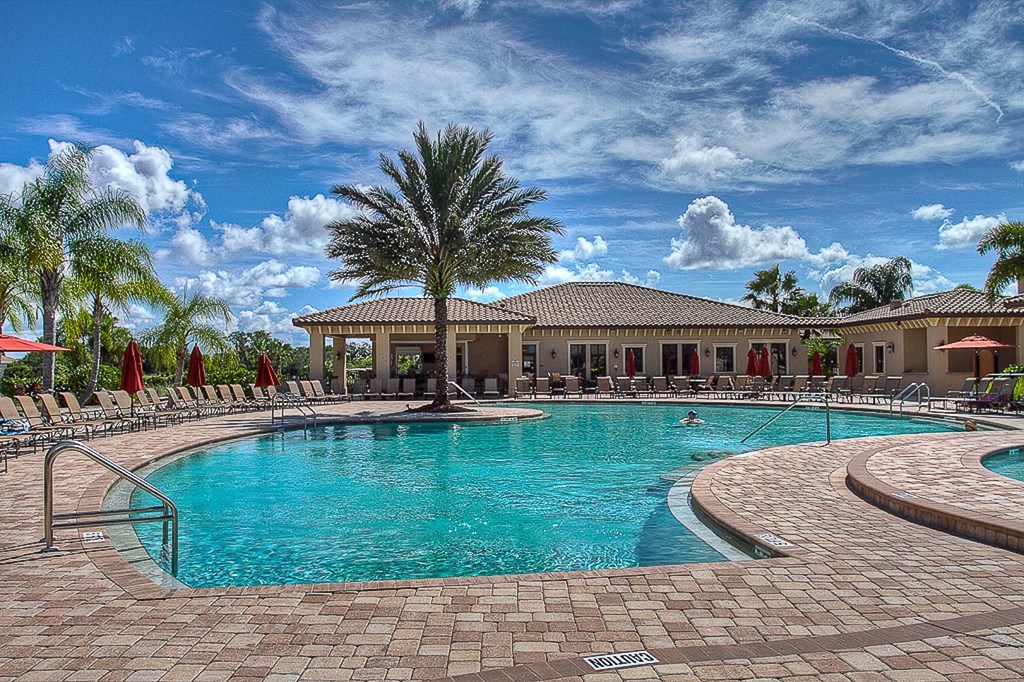 A large swimming pool surrounded by a brick patio and red umbrellas.