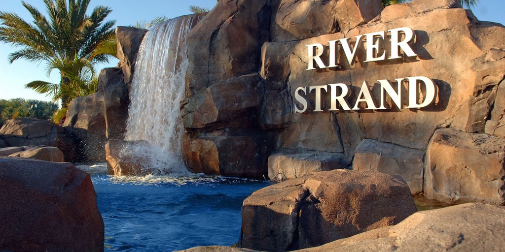 A waterfall flows into a pool in front of a rock with the words "River Strand" written on it.