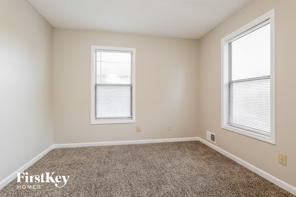 a spacious room with carpet and two windows