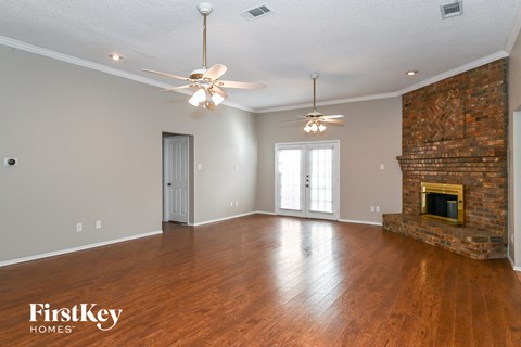 an empty living room with a fireplace and two ceiling fans