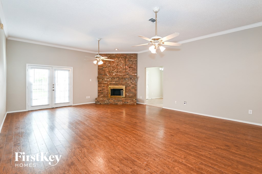 an empty living room with a fireplace and two ceiling fans