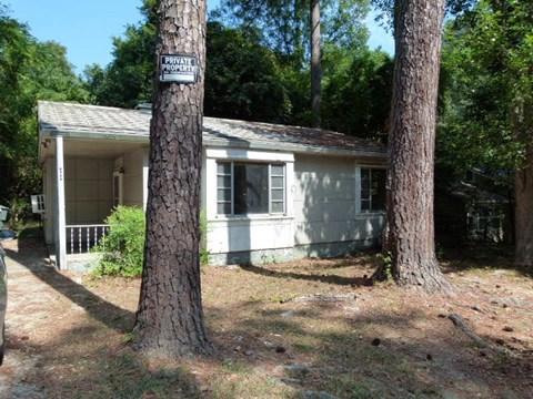 A small house with a porch is surrounded by trees and has a sign that says "PRIVATE PROPERTY".