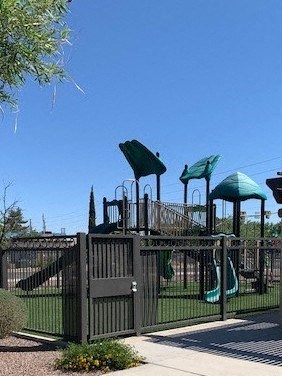 A playground with a green slide and a black fence.