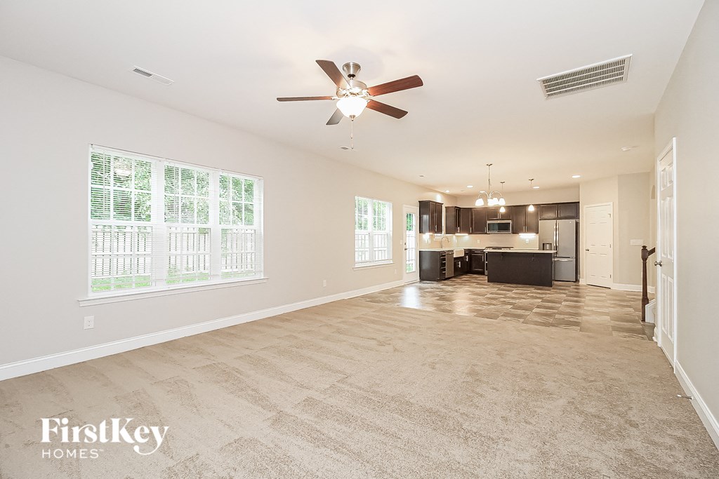 an empty living room with a ceiling fan and a kitchen