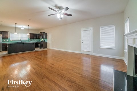 an empty living room and kitchen with wood flooring and a ceiling fan