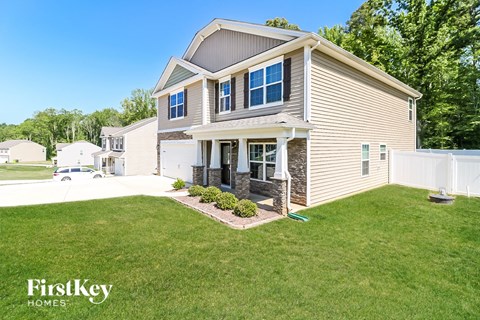 a beige house with a lawn and a white fence
