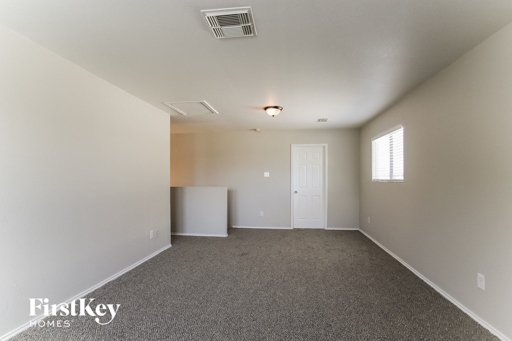 A spacious room with a carpeted floor and a window on the right side.