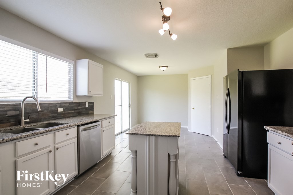 A kitchen with a black fridge and a sink with a granite counter top.