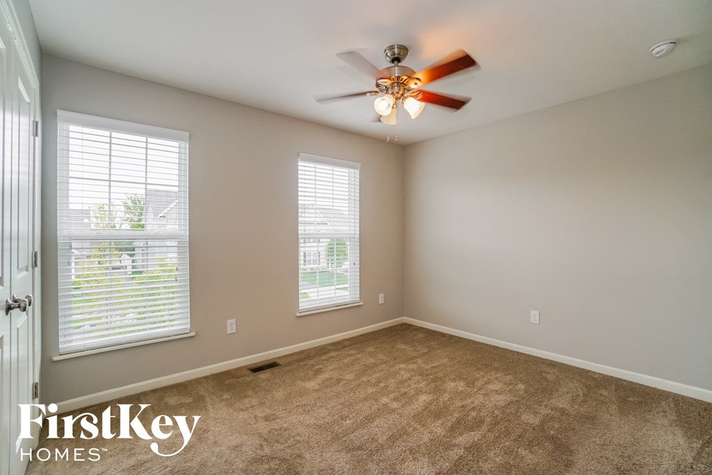 an empty room with a ceiling fan and two windows