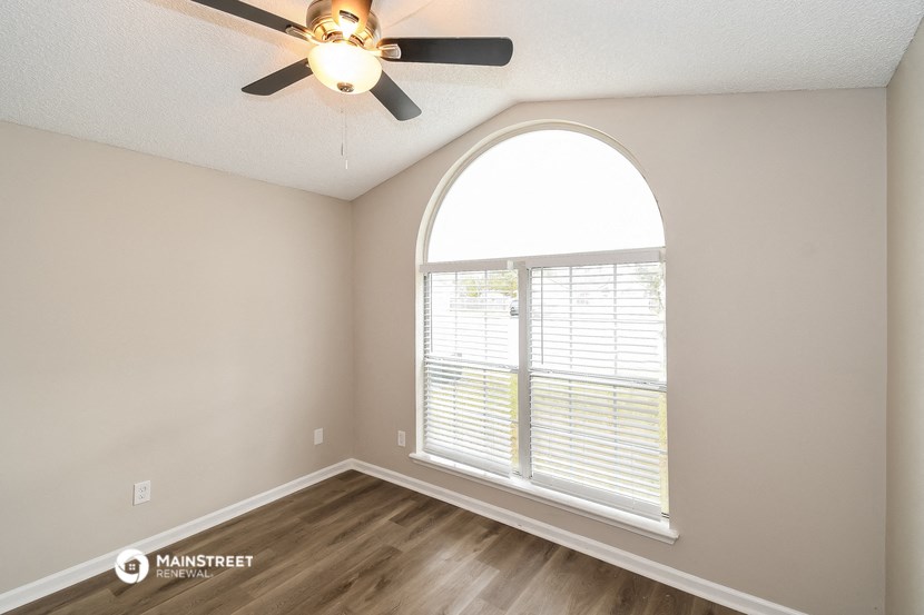 the spacious living room with a large window and a ceiling fan