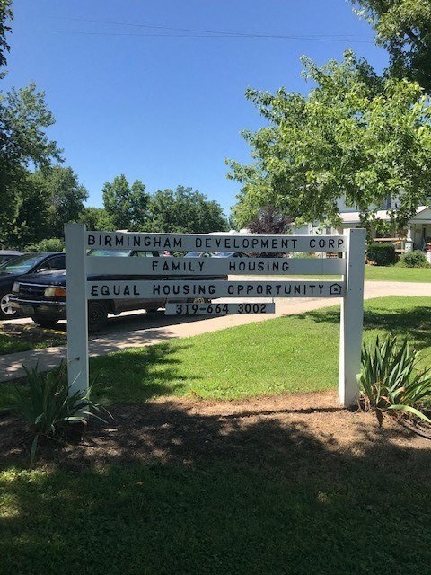 a sign in the grass in front of a parking lot