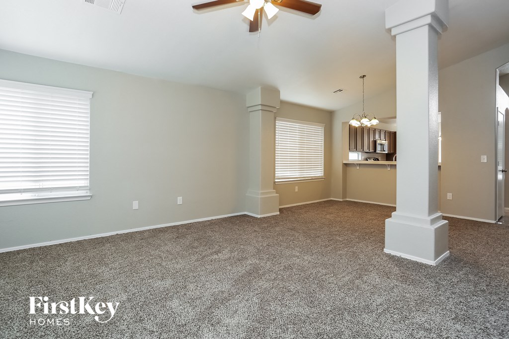 A spacious room with a carpeted floor, a ceiling fan, and a pillar.