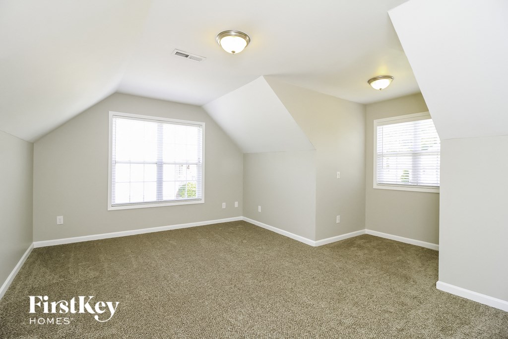 A spacious room with a carpeted floor and two windows.