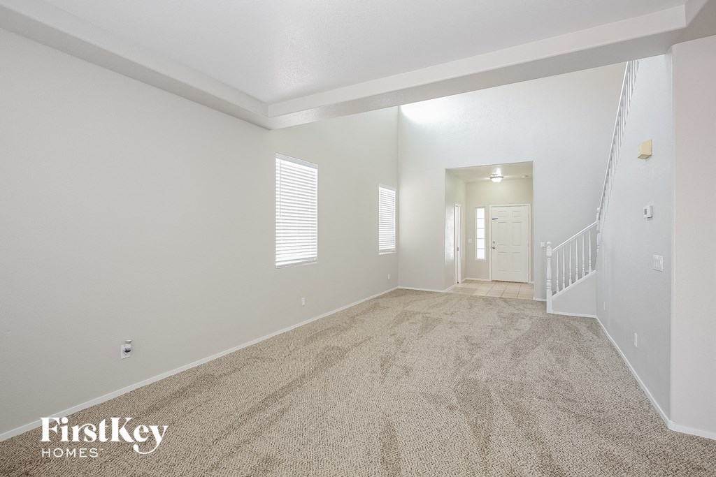 a spacious living room with carpeted flooring and a white door to the hallway