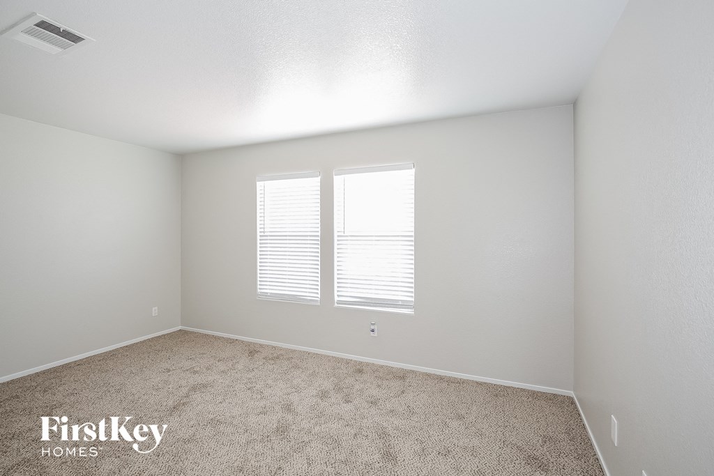 a bedroom with white walls and carpet and two windows