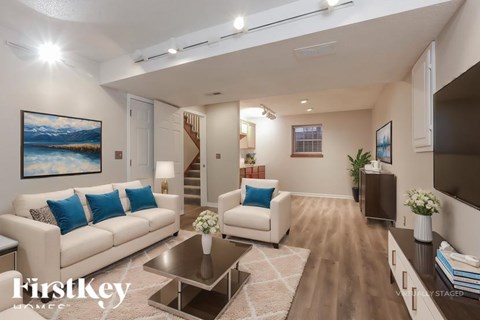 A well-lit living room with a white sofa and a painting on the wall.