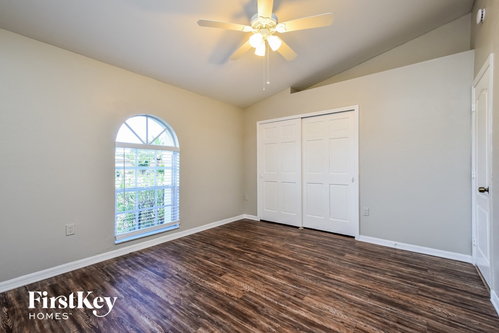 the spacious living room with hardwood flooring and a ceiling fan