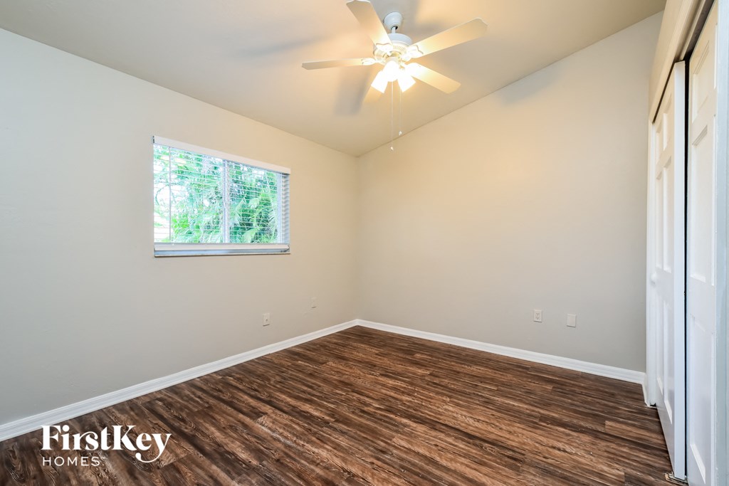 the spacious living room with hardwood flooring and a ceiling fan