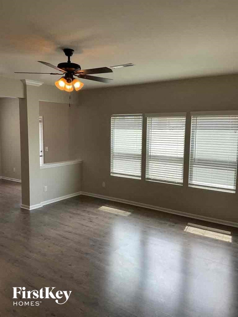 an empty living room with a ceiling fan and three windows