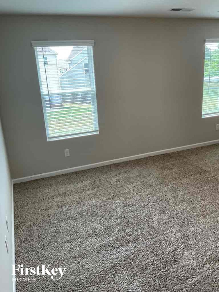 a carpeted room with two windows and a gray wall