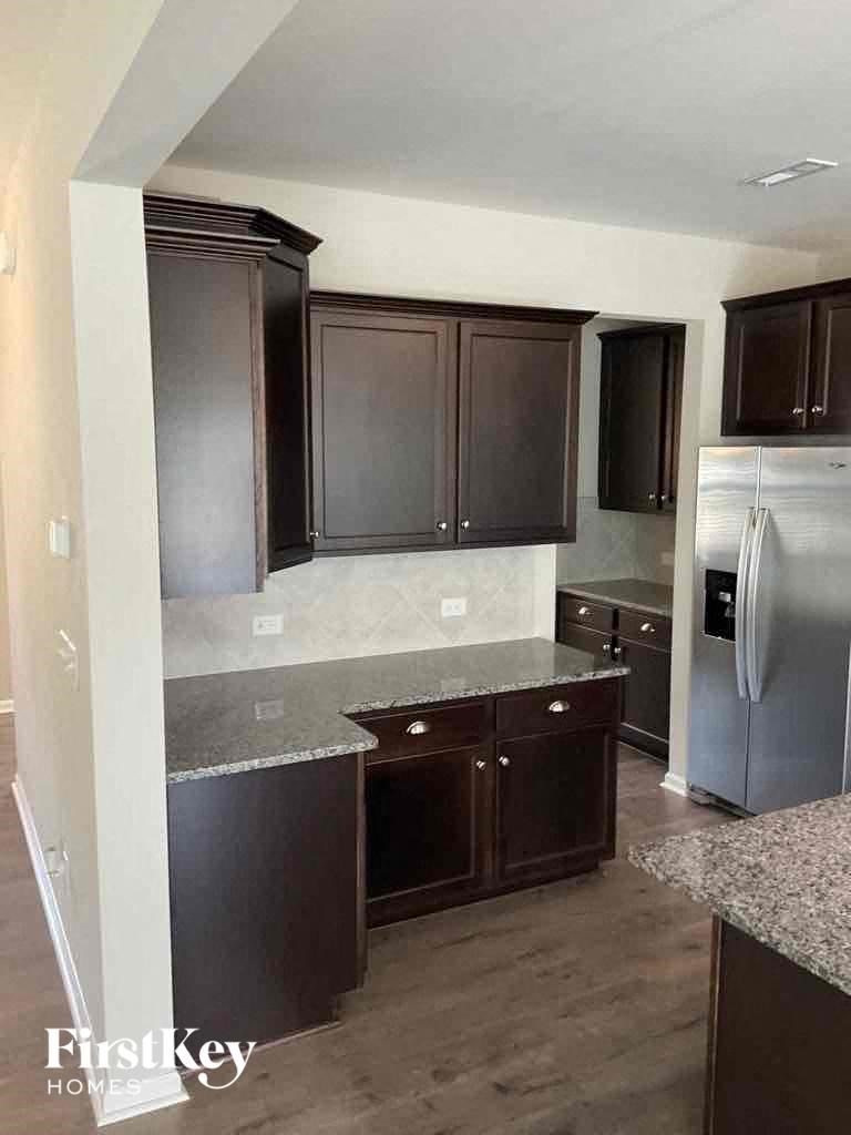 an empty kitchen with dark cabinets and stainless steel refrigerator