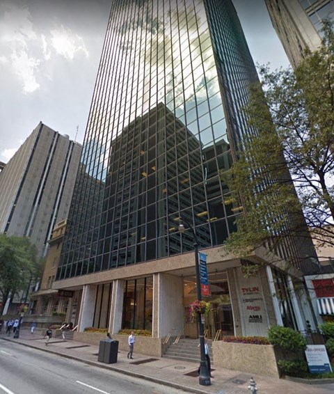A tall building with a glass facade stands in front of a tree.