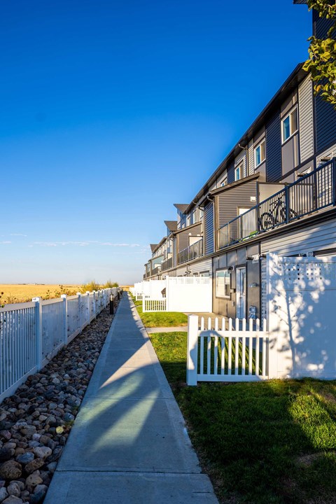 a sidewalk in front of an apartment building with a white fence