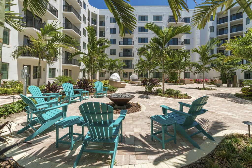 a patio with chairs and a fire pit in front of an apartment building