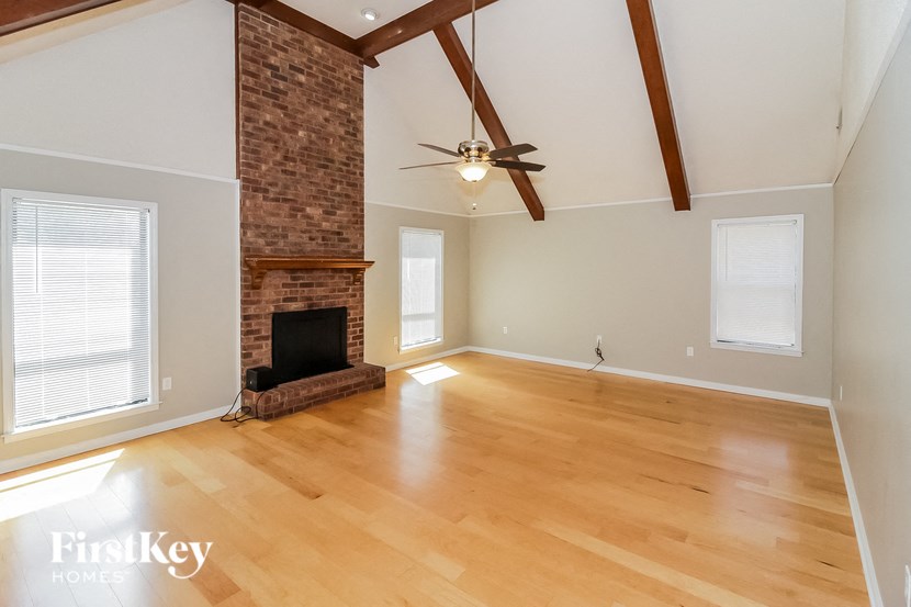 a living room with a brick fireplace and wooden floors and a ceiling fan