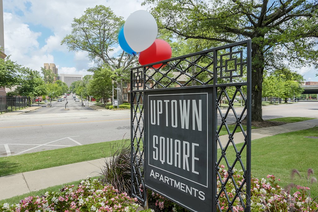 a sign for uptown square apartments in front of a garden with balloons