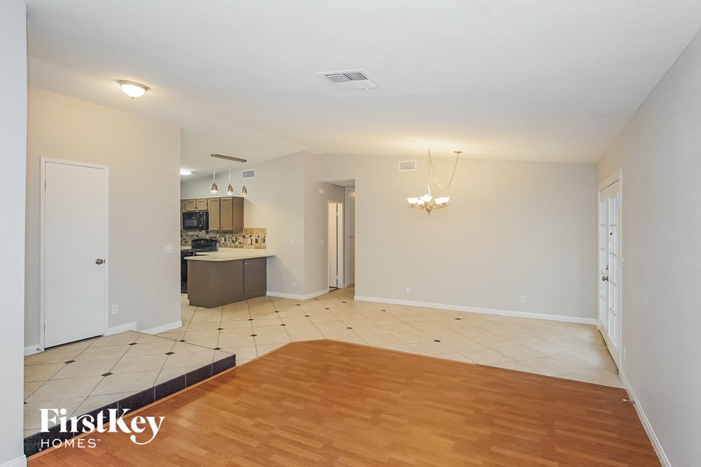 A room with a wooden floor and a kitchen area in the background.