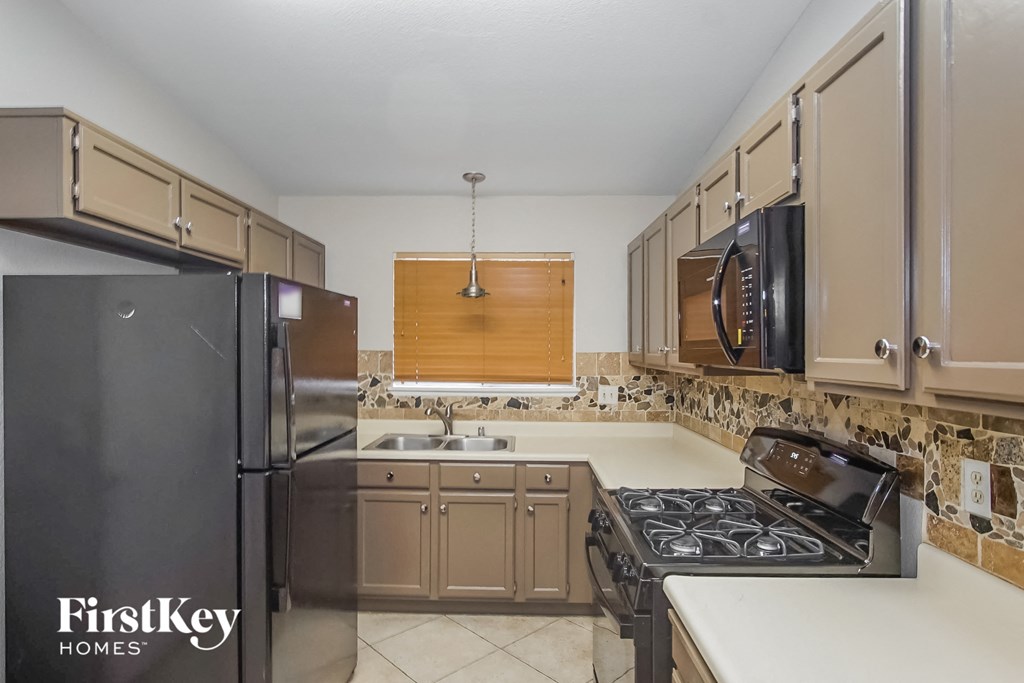 A kitchen with a black refrigerator and a stove top oven.