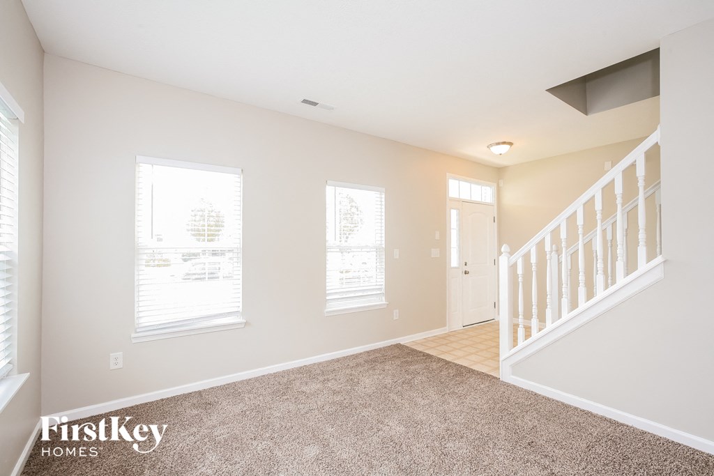 the living room and entryway of a home with carpeted floors and a staircase