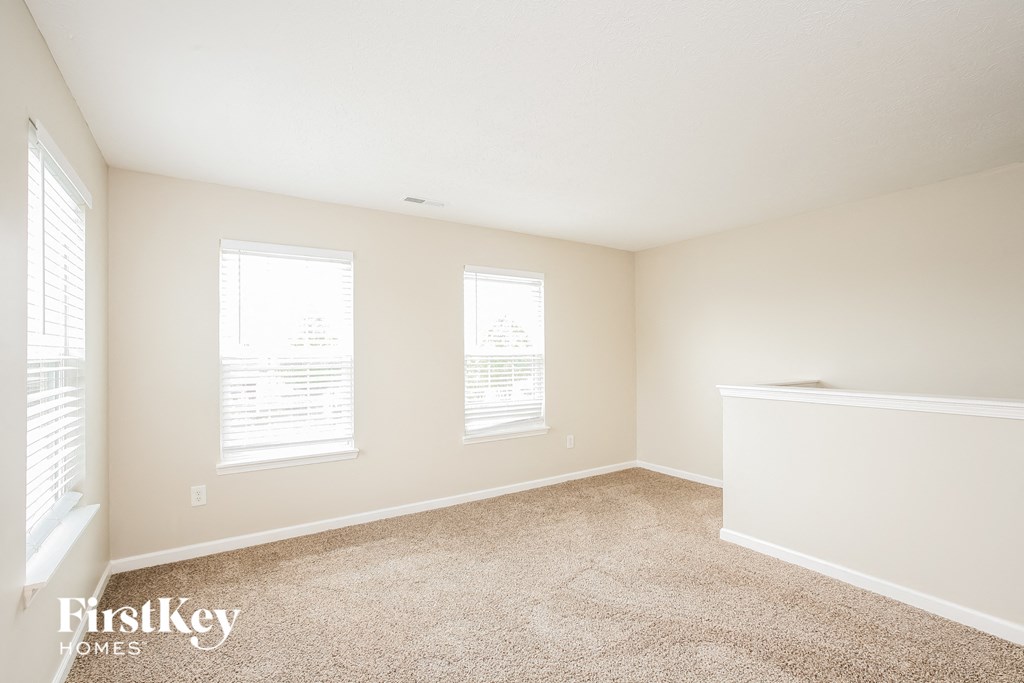 a spacious living room with carpet and three windows