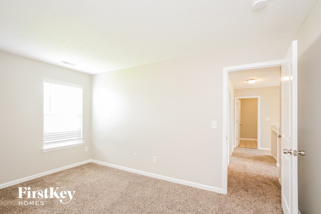 a bedroom with white walls and carpet and a door to a hallway
