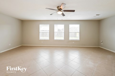 an empty living room with a ceiling fan and three windows