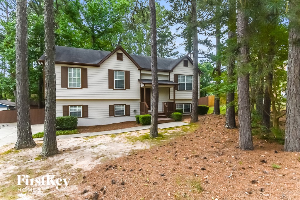 A house with a brown roof and white siding is surrounded by trees.