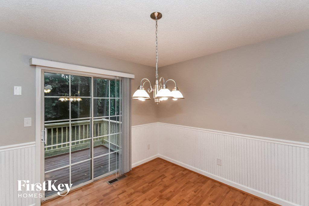 A room with a wooden floor, a chandelier, and a sliding glass door leading to a deck.