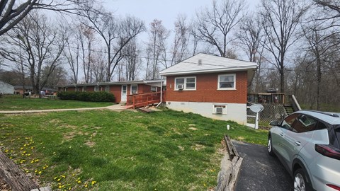 A house with a red brick exterior and a white roof is surrounded by a grassy area and trees.