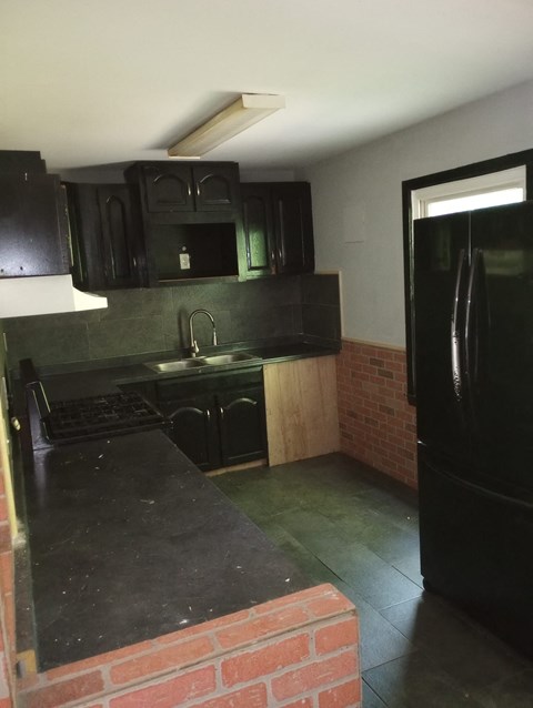 A kitchen with black cabinets and a brick wall.
