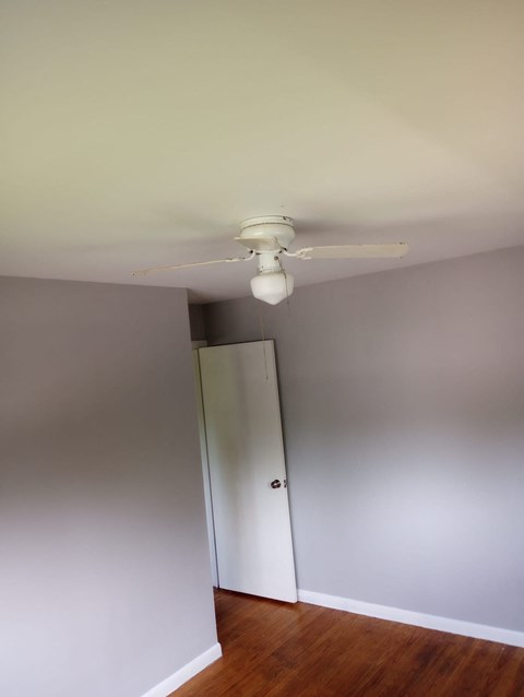 A white ceiling fan hangs from a ceiling in a room with a wooden floor and white walls.
