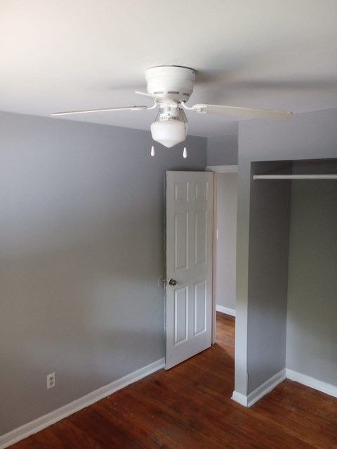 A white ceiling fan hangs over a wood floor in a room.